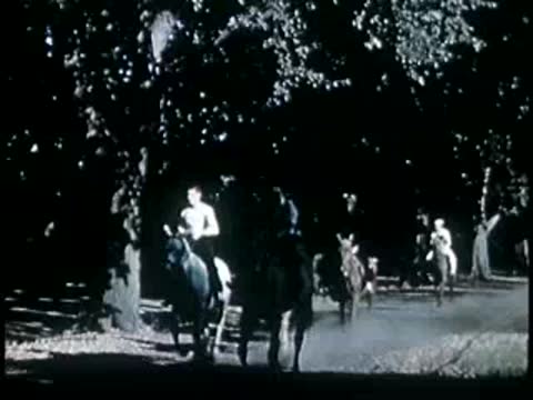 People riding horses along a wooded trail shaded by trees, mid-20th century.