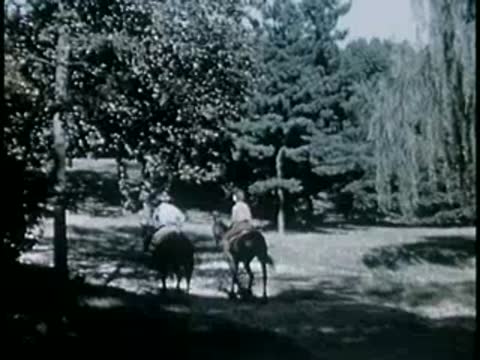 Two horseback riders traveling through a grassy park area with trees, 1940s.