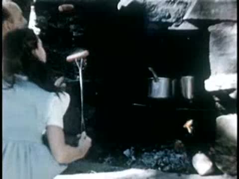 Young girl cooking food over an open campfire outdoors, mid-20th century.