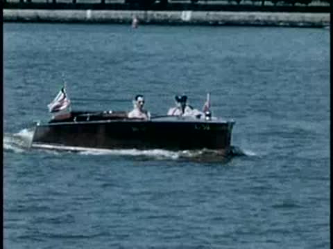 Motorboat cruising across open water with American flags flying, mid-20th century.