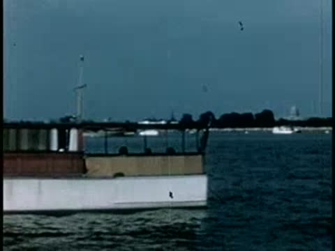 Cabin cruiser boat moving across a lake near a distant shore, 1940s.