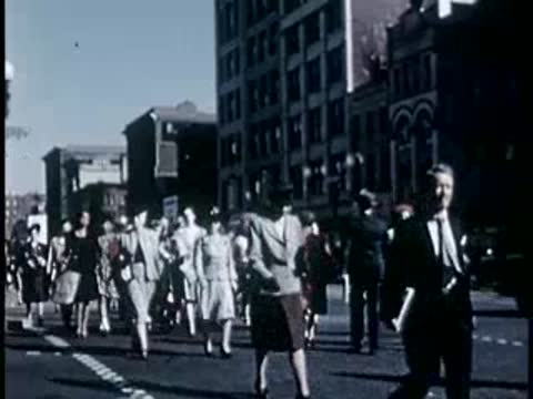 Crowd of people walking briskly on city street, 1940s film style