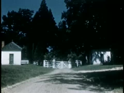 Country road leading toward white gates and outbuildings