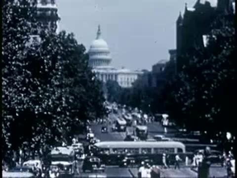 Medium tracking shot down a busy street toward the U.S. Capitol dome, 1940s.