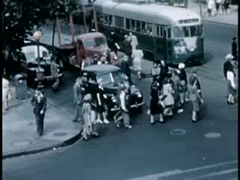 Pedestrians crossing a busy intersection with streetcars and cars, 1940s era.