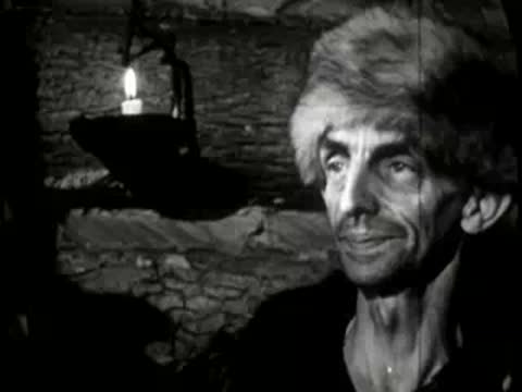 man with fur hat talking or singing by candlelight indoors