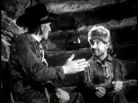 two men sitting and talking inside a log cabin interior