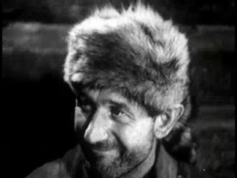man wearing a fur hat smiling indoors by candlelight