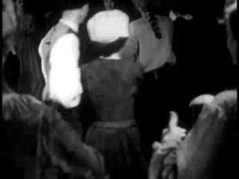 people folk dancing indoors in a crowded rustic room