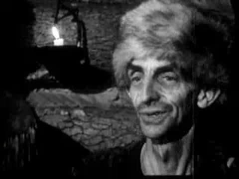 man with fur hat talking or gesturing indoors by candlelight