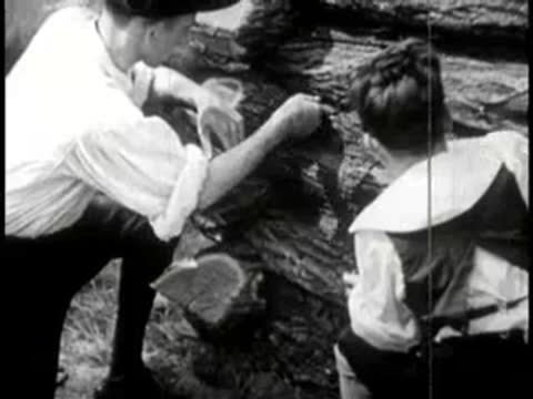 Two men mud-chinking a log cabin wall in daylight.