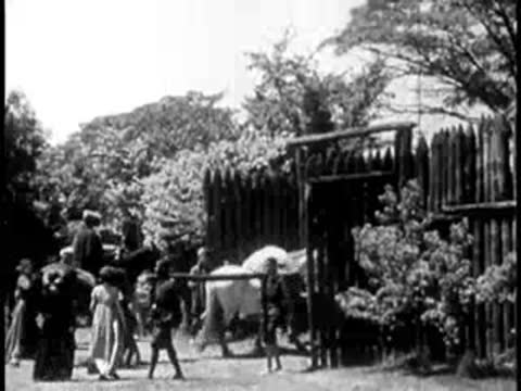 Settlers and livestock entering through the gates of a stockade fort.