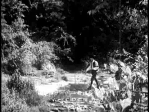 Pioneers walking across a shallow rocky stream in a wooded landscape