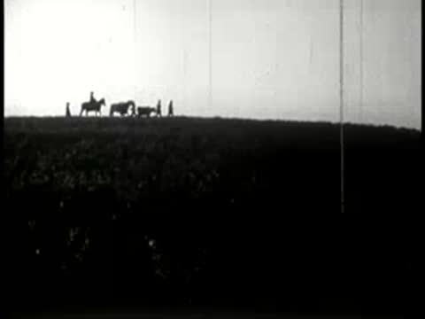 Settlers with livestock walking along a hill ridge against the sky.