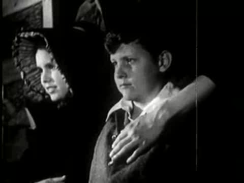 A close-up of a young girl and boy looking out a doorway.