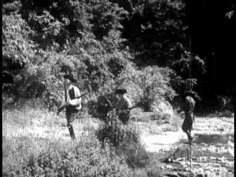 Pioneers carrying muskets walking along a rocky forest path