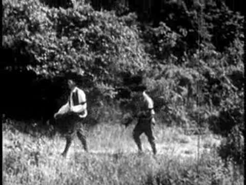 Pioneers with muskets walking through tall grass and trees