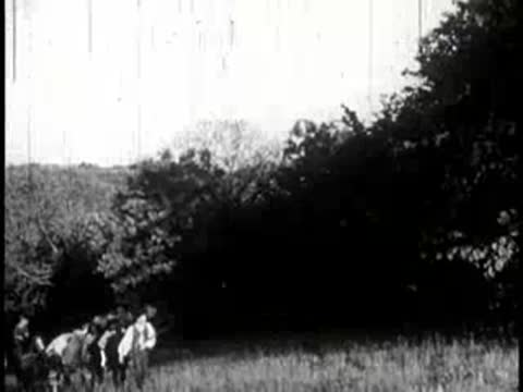 Distant view of pioneers walking with pack animals across an open field