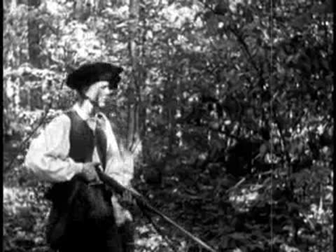 Two pioneers standing with muskets in a wooded clearing talking