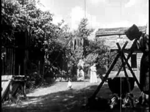 Outdoor chores at a settlement with a large cauldron and people working.