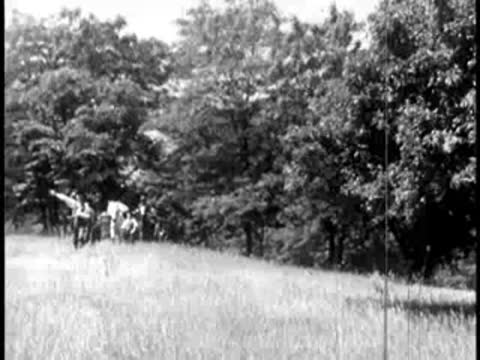 Group of pioneers walking across an open grassy field near a treeline.