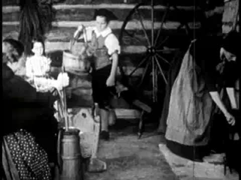 Boy churning butter inside a rustic log cabin kitchen interior.