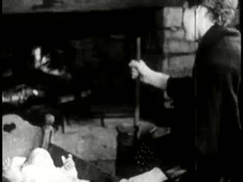 Woman stirring a pot over an open fireplace with an infant cradle nearby.
