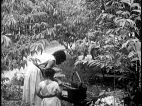 a woman and a child working outdoors near vegetation and a small structure