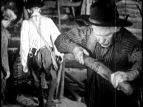 a man in a hat working with a wooden log or tool in a workshop