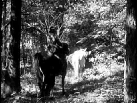 Pioneers riding horses through a wooded trail carrying supplies