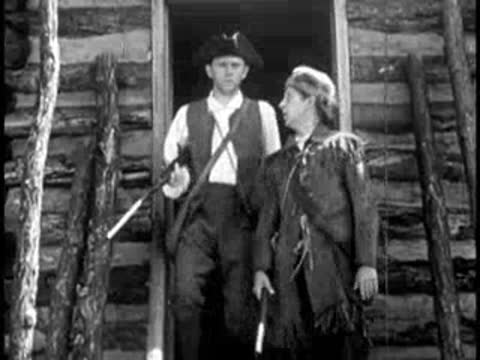 a man with a rifle stepping out of a rustic log cabin doorway