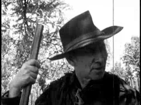 close-up of a man in a hat holding a long rifle outdoors