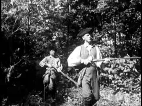 Pioneers carrying muskets walking through a dense forest trail