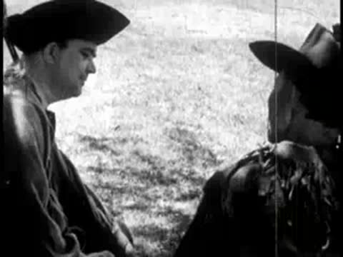 two men sitting and talking outdoors with a dog nearby in the grass