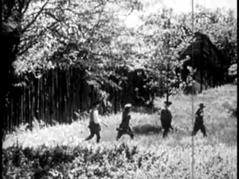 Group of people walking towards a rustic cabin along a wooden fence