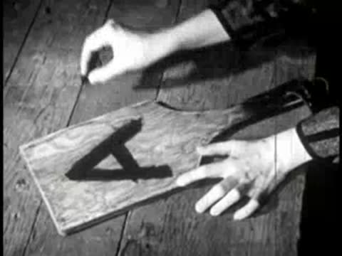 Hands writing the letter A on a wooden slate paddle with chalk