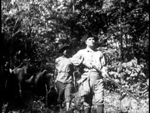 Pioneers with muskets walking through a forest with pack animals behind them