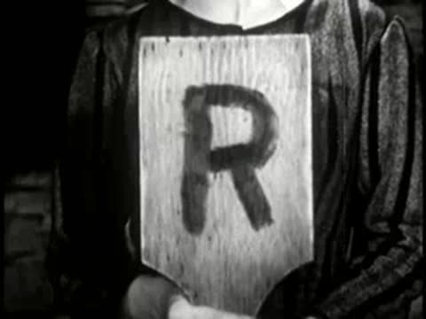 A person holding up a wooden paddle with the letter R painted on it