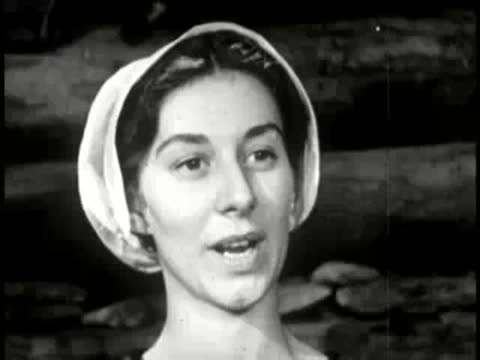 A woman speaking in a rustic log cabin interior