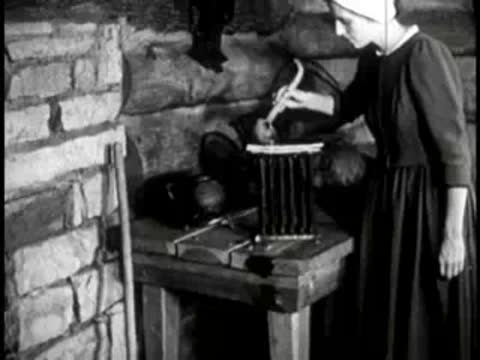 A woman working near a fireplace and wooden table inside a cabin