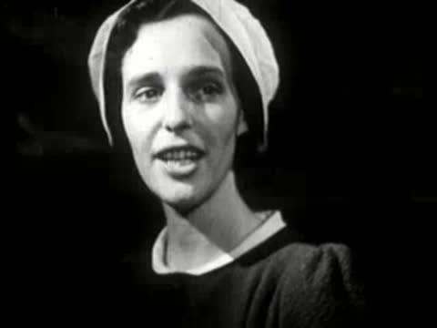 A woman wearing a bonnet speaking inside a wooden cabin