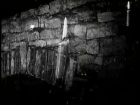 A lit candle burning against a stone wall in a cabin