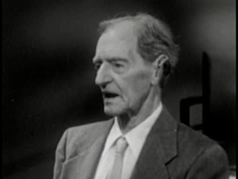 Elderly man in suit speaking, vintage television studio interview setting.