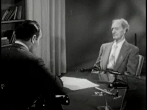 Two men sitting at desk, vintage television studio interview setting.