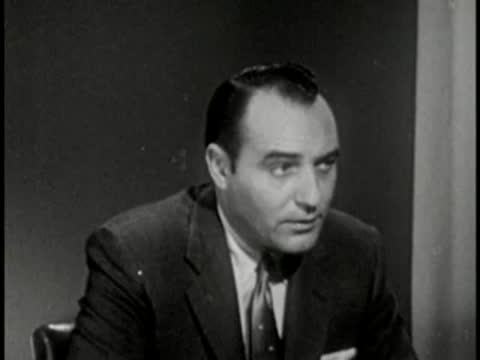 Man in suit and tie talking, interview setting, vintage tv broadcast.