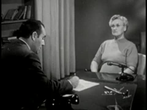 Man interviewing older woman across desk, office setting, vintage broadcast.
