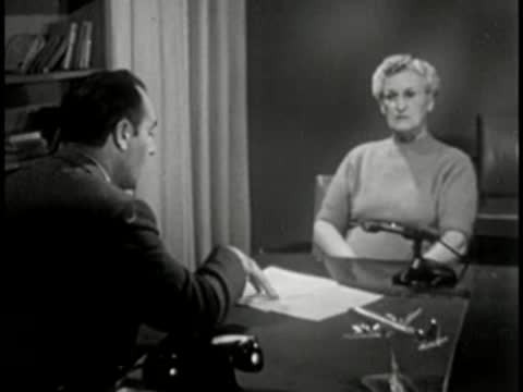 Man interviewing older woman across desk, office setting, vintage broadcast.