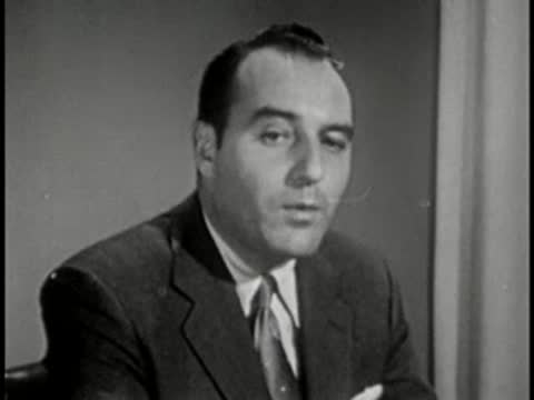 Man in suit and tie speaking, interview setting, vintage tv broadcast.
