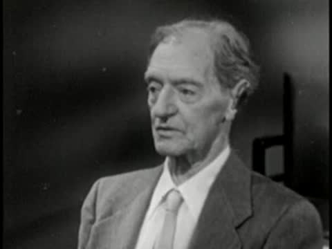 Elderly man in suit speaking, vintage television studio interview setting.
