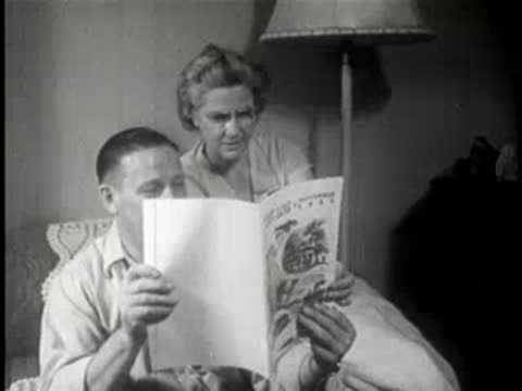 Man and woman sitting indoors, reading a magazine together in a living room